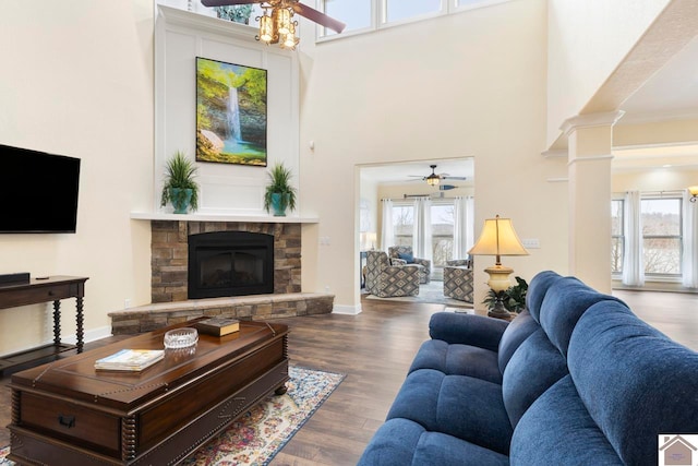 living room with ceiling fan, decorative columns, a fireplace, a towering ceiling, and wood finished floors