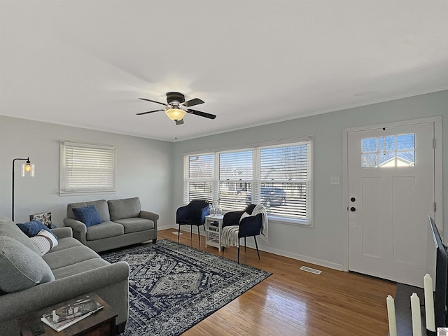 living area featuring visible vents, crown molding, baseboards, wood finished floors, and a ceiling fan