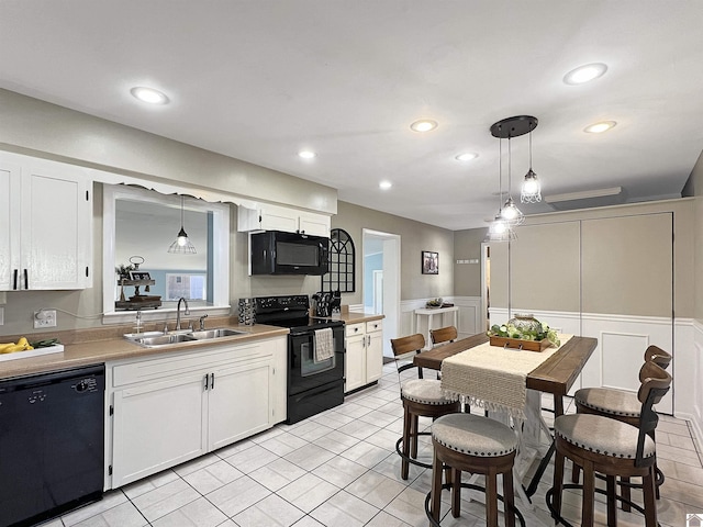 kitchen with a sink, white cabinetry, black appliances, and hanging light fixtures