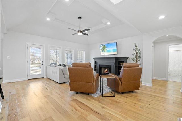 living area with light wood-type flooring, a warm lit fireplace, recessed lighting, arched walkways, and baseboards