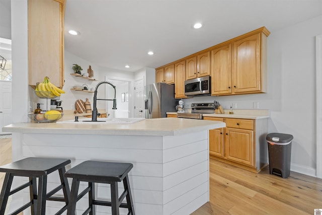 kitchen featuring a breakfast bar area, light wood finished floors, a peninsula, stainless steel appliances, and light countertops