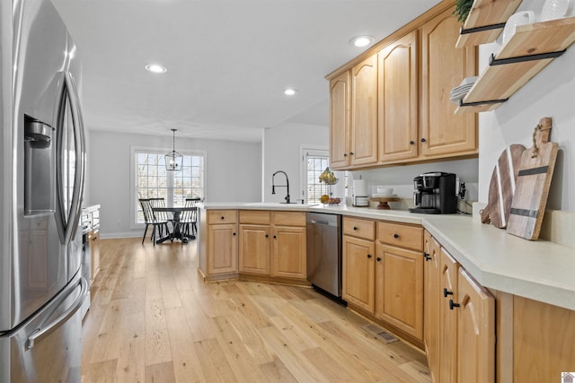 kitchen featuring a sink, stainless steel appliances, light wood-style floors, a peninsula, and light countertops