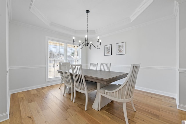 dining room with a tray ceiling, crown molding, light wood-type flooring, and baseboards