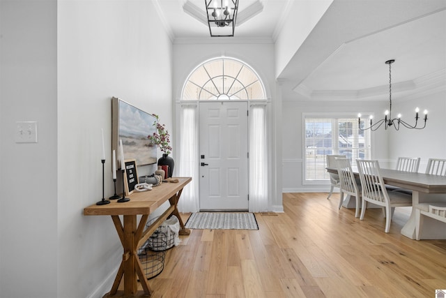 entryway featuring ornamental molding, a tray ceiling, an inviting chandelier, light wood finished floors, and baseboards