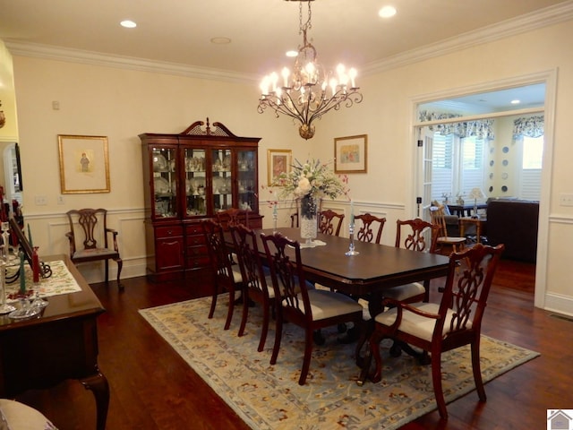 dining room with crown molding, dark wood-type flooring, wainscoting, an inviting chandelier, and a decorative wall