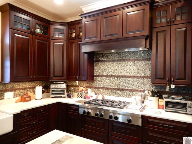 kitchen featuring under cabinet range hood, backsplash, stainless steel gas stovetop, and light countertops