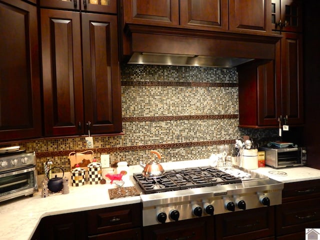 kitchen featuring wall chimney range hood, backsplash, stainless steel gas stovetop, and light countertops