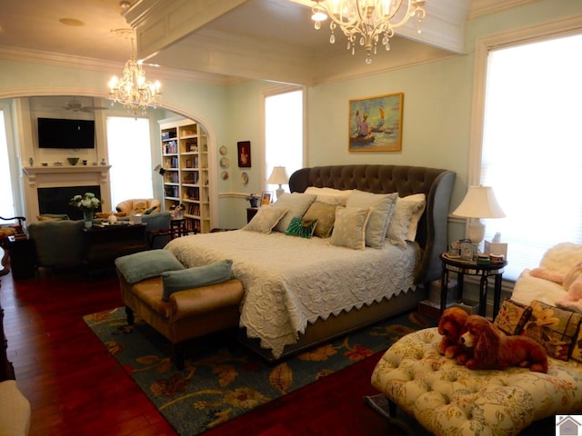 bedroom featuring a fireplace, an inviting chandelier, wood finished floors, and crown molding