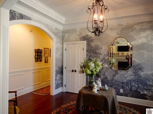 dining room featuring a notable chandelier, ornamental molding, wood finished floors, arched walkways, and wallpapered walls