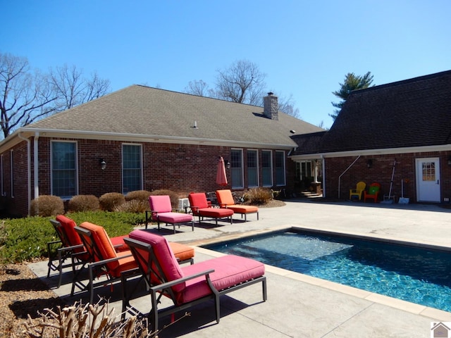 back of property featuring a patio area, an outdoor pool, a chimney, and brick siding