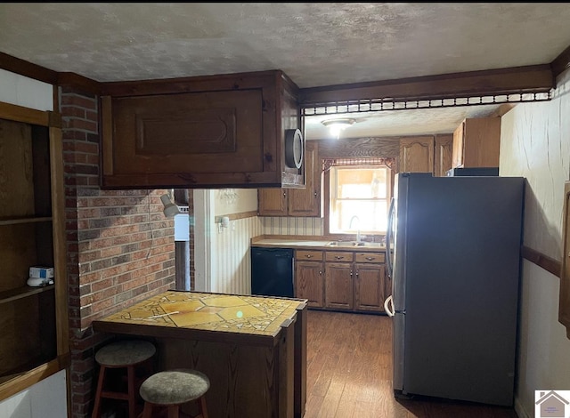 kitchen with dishwasher, light wood-type flooring, freestanding refrigerator, a textured ceiling, and a sink