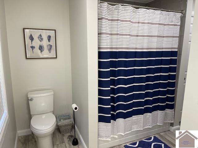 full bathroom with a shower with shower curtain, toilet, wood finished floors, and baseboards