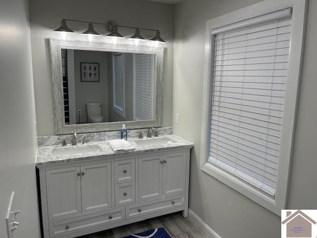 bathroom with double vanity, toilet, baseboards, and a sink