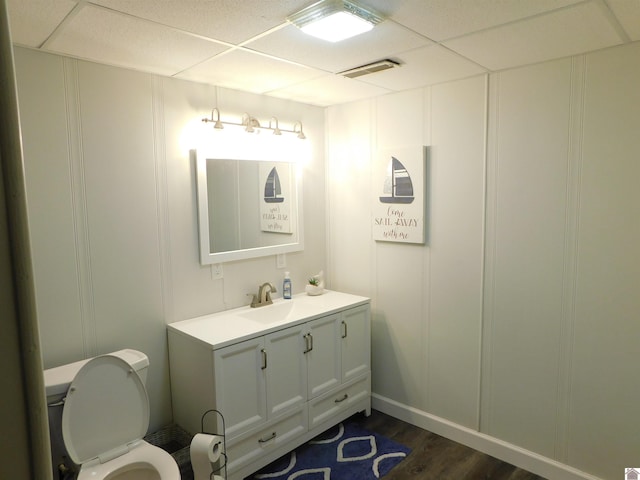 half bathroom with vanity, wood finished floors, visible vents, a decorative wall, and toilet