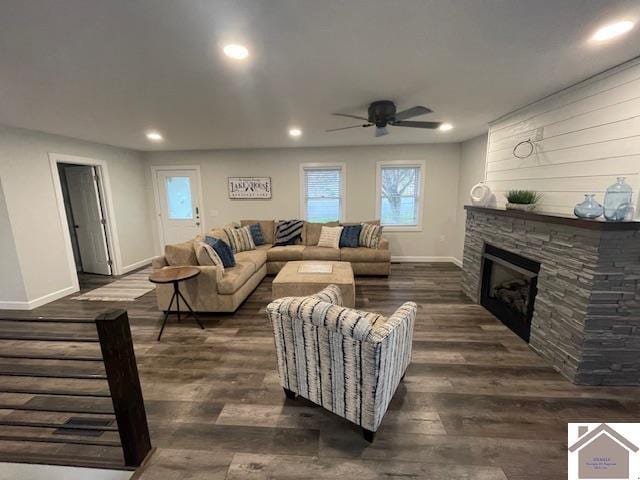 living room featuring a stone fireplace, recessed lighting, dark wood-style floors, and baseboards