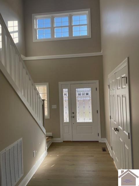 entryway featuring stairway, baseboards, visible vents, a towering ceiling, and light wood-type flooring