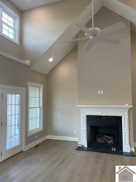 unfurnished living room featuring baseboards, a fireplace, wood finished floors, high vaulted ceiling, and a ceiling fan