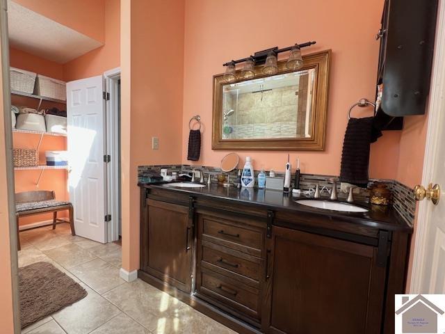 full bath featuring tile patterned floors, double vanity, baseboards, and a sink