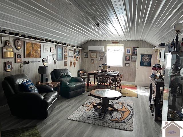 living room featuring vaulted ceiling, wood finished floors, and a wall mounted AC