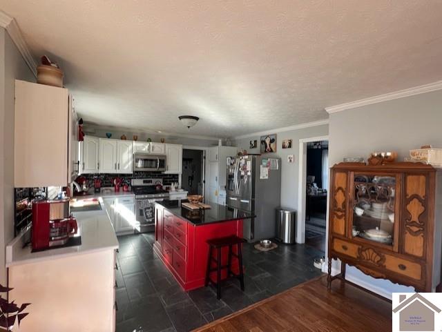 kitchen with a sink, a center island, appliances with stainless steel finishes, white cabinets, and crown molding