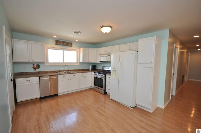 kitchen featuring visible vents, a sink, stainless steel appliances, light wood-style floors, and dark countertops