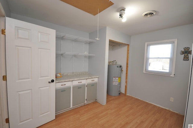 clothes washing area featuring water heater, visible vents, attic access, and light wood-type flooring