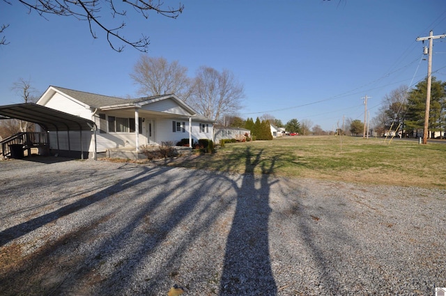 view of side of property with gravel driveway, a porch, a yard, and a detached carport