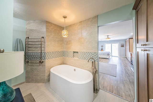 bathroom with radiator, tile patterned floors, a soaking tub, tile walls, and a ceiling fan