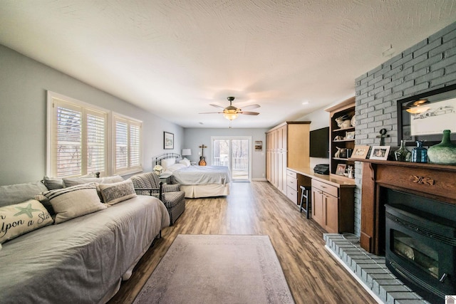 bedroom with ceiling fan, a textured ceiling, wood finished floors, and a fireplace