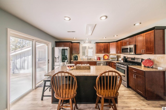 kitchen with light wood-type flooring, stainless steel appliances, a kitchen breakfast bar, and a kitchen island