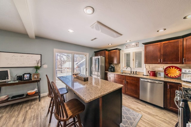 kitchen featuring a sink, backsplash, appliances with stainless steel finishes, a breakfast bar area, and light stone countertops