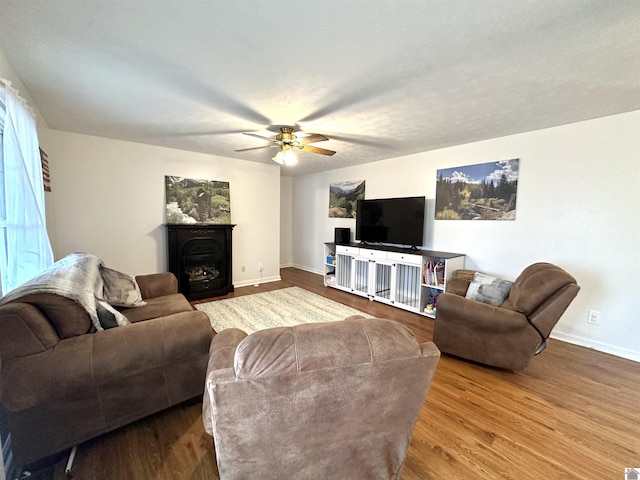 living area with a fireplace, a ceiling fan, baseboards, and wood finished floors