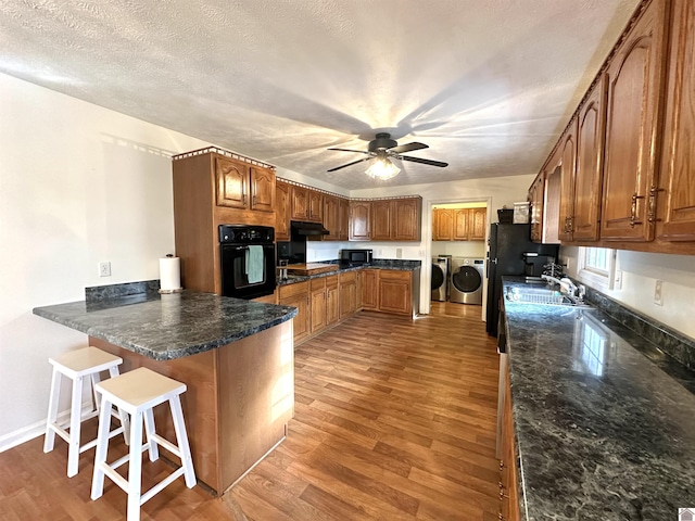 kitchen with washer and clothes dryer, a peninsula, black appliances, and light wood-type flooring