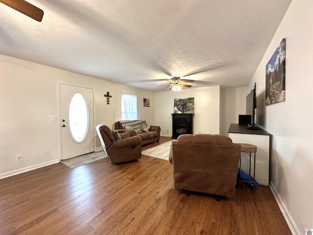 living room with a ceiling fan, wood finished floors, baseboards, and a textured ceiling