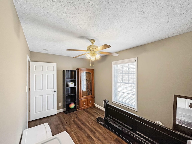 interior space featuring ceiling fan, a textured ceiling, baseboards, and dark wood-style flooring