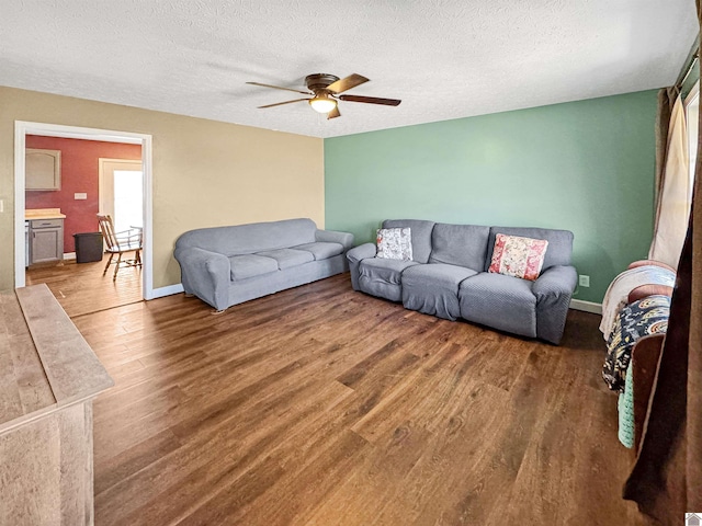 living area with ceiling fan, wood finished floors, baseboards, and a textured ceiling