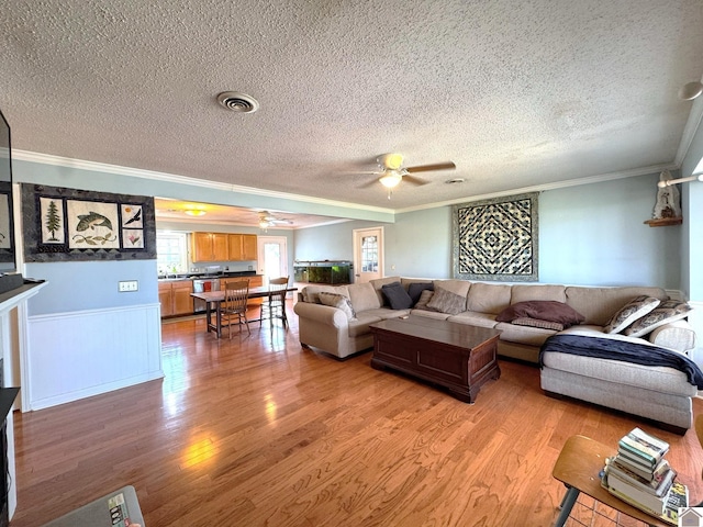 living area with light wood-type flooring, visible vents, ceiling fan, and ornamental molding