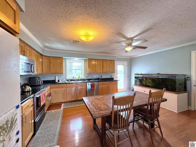 kitchen with dark countertops, appliances with stainless steel finishes, crown molding, and wood-type flooring