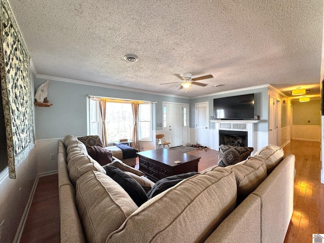 living area with visible vents, a fireplace, ceiling fan, wood-type flooring, and crown molding