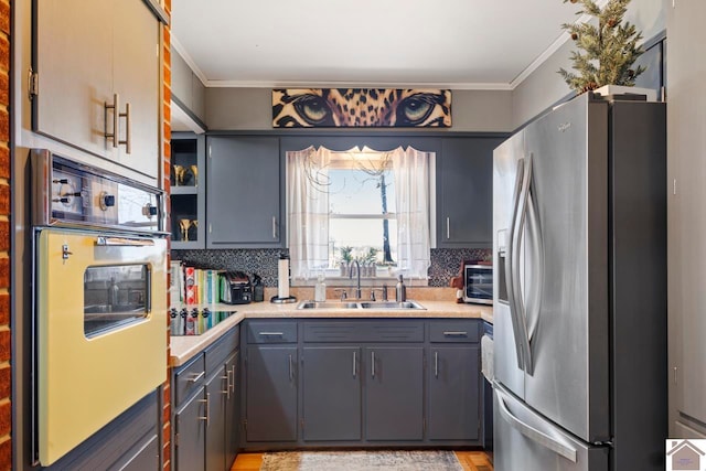 kitchen with oven, ornamental molding, a sink, stainless steel fridge, and backsplash