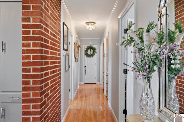 hallway featuring light wood finished floors, brick wall, baseboards, a chandelier, and ornamental molding