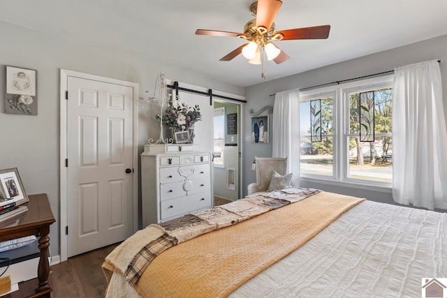 bedroom with a barn door, ceiling fan, and dark wood-style flooring