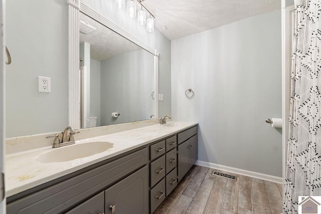 full bath with a sink, a textured ceiling, wood finished floors, and double vanity