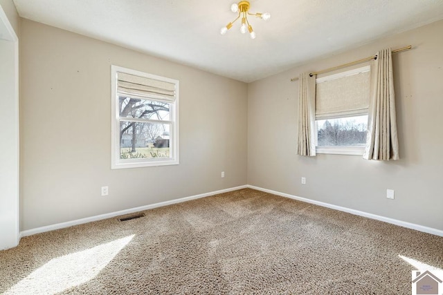 carpeted spare room featuring visible vents, plenty of natural light, baseboards, and a chandelier