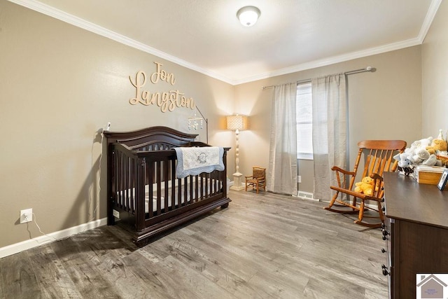 bedroom with a nursery area, crown molding, baseboards, and wood finished floors