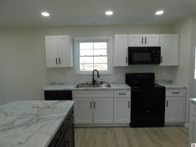 kitchen with a sink, light wood-type flooring, black appliances, and white cabinetry