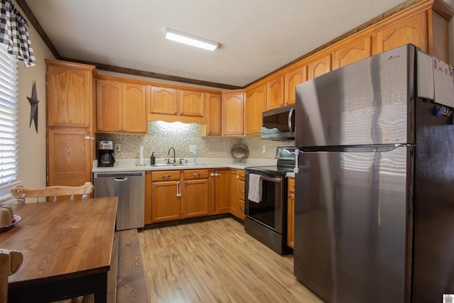 kitchen featuring backsplash, light countertops, light wood-style flooring, appliances with stainless steel finishes, and a sink