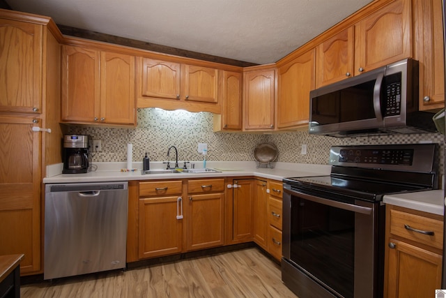 kitchen featuring stainless steel appliances, light countertops, light wood-style floors, and a sink