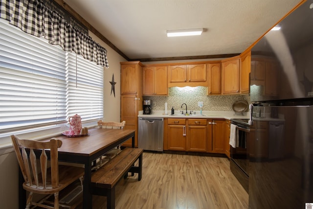 kitchen with light wood finished floors, backsplash, light countertops, black appliances, and a sink