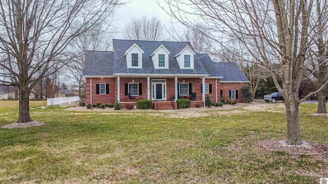 new england style home with brick siding, roof with shingles, a front yard, and fence